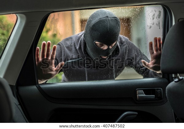 Man dressed in black with a balaclava on\
his head looking through car window and wondering how to break into\
this car. Car thief, car theft\
concept