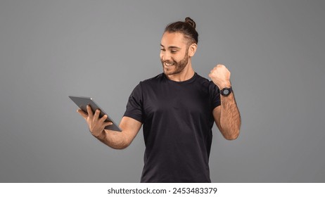 A man dressed in a black shirt is standing while holding a tablet in his hands. He appears focused on the screen, engrossed in whatever he is viewing or working on - Powered by Shutterstock