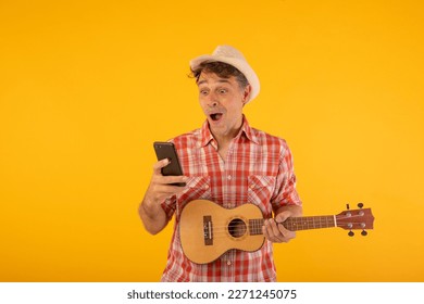 Man dressed in a cheerful and youthful way using his mobile phone and carrying a ukulele - Powered by Shutterstock