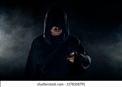 Man Dressed In A Dark Robe Looking Like A Cult Leader On A Smoky Or Foggy Background.  He Looks Like A Creepy Evil Villain