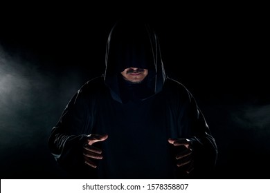 Man Dressed In A Dark Robe Looking Like A Cult Leader On A Smoky Or Foggy Background.  He Looks Like A Creepy Evil Villain