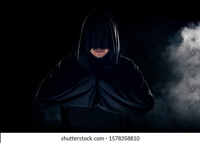 Man Dressed In A Dark Robe Looking Like A Cult Leader On A Smoky Or Foggy Background.  He Looks Like A Creepy Evil Villain