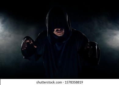 Man Dressed In A Dark Robe Looking Like A Cult Leader On A Smoky Or Foggy Background.  He Looks Like A Creepy Evil Villain