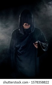 Man Dressed In A Dark Robe Looking Like A Cult Leader On A Smoky Or Foggy Background.  He Looks Like A Creepy Evil Villain