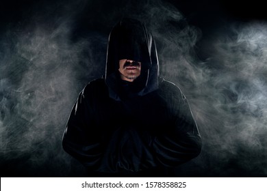 Man Dressed In A Dark Robe Looking Like A Cult Leader On A Smoky Or Foggy Background.  He Looks Like A Creepy Evil Villain