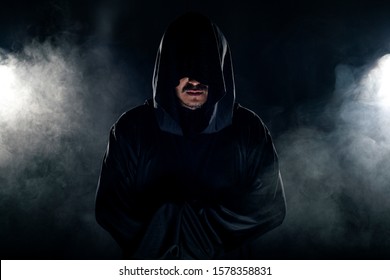 Man Dressed In A Dark Robe Looking Like A Cult Leader On A Smoky Or Foggy Background.  He Looks Like A Creepy Evil Villain