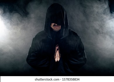 Man Dressed In A Dark Robe Looking Like A Cult Leader On A Smoky Or Foggy Background.  He Looks Like A Creepy Evil Villain