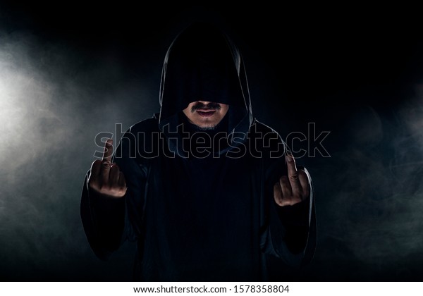 Man dressed in a dark robe looking like a cult leader on a smoky or foggy background.  He looks like a creepy evil villain