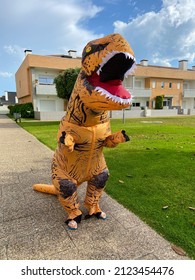 A Man Dressed In A Dinosaur Costume. T-REX Dinosaur Inflatable Halloween Costume. One Big And Tall Dinosaur Enjoying And Having Fun.