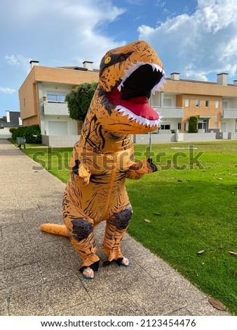 A man dressed in a dinosaur costume. T-REX Dinosaur Inflatable Halloween costume. One big and tall dinosaur enjoying and having fun.