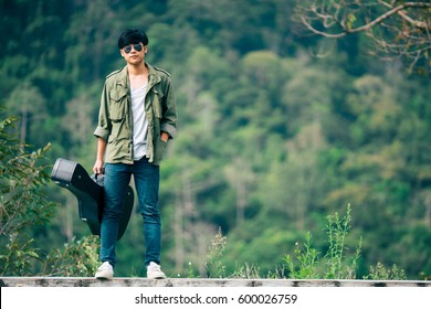 Man Dressed In Jeans Holding Guitar Case In Nature Outdoor.