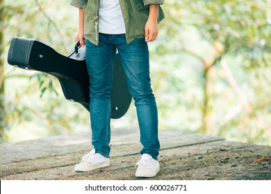 Man Dressed In Jeans Holding Guitar Case In Nature Outdoor.