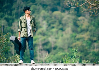 Man Dressed In Jeans Holding Guitar Case In Nature Outdoor.