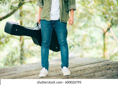 Man Dressed In Jeans Holding Guitar Case In Nature Outdoor.