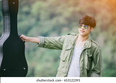 Man Dressed In Jeans Holding Guitar Case In Nature Outdoor.