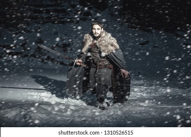 Man Dressed In Medieval Armor And Raincoats With Swords In Winter In The Mountains Under Heavy Snow Blizzard. Fantasy Warrior Knights In Winter Snowy Landscape