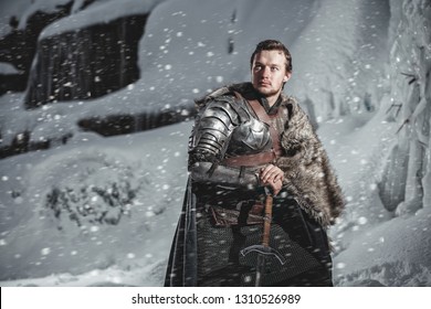 Man Dressed In Medieval Armor And Raincoats With Swords In Winter In The Mountains Under Heavy Snow Blizzard. Fantasy Warrior Knights In Winter Snowy Landscape