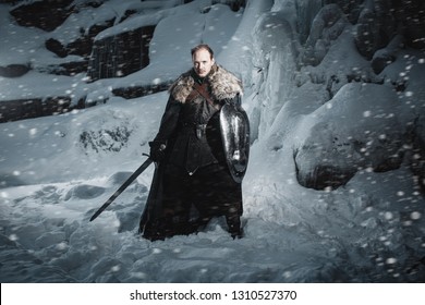 Man Dressed In Medieval Armor And Raincoats With Swords In Winter In The Mountains Under Heavy Snow Blizzard. Fantasy Warrior Knights In Winter Snowy Landscape