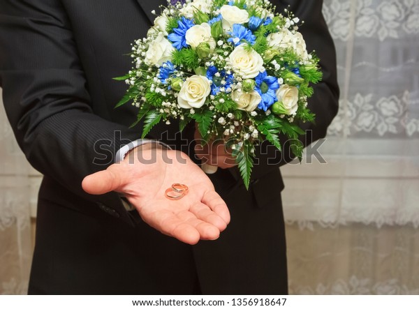 Man dressed in a suit with a bouquet of flowers,\
dividing the rings on the\
palm