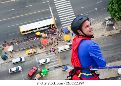 Man dressed as a superhero rappelling down from a tall building. Salvador Bahia Brazil.