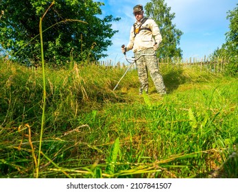 A man dressed in work clothes is using a gasoline mower to cut long grass. Summer. rural area, maintenance of the territory. Grass mowing, modern technologies