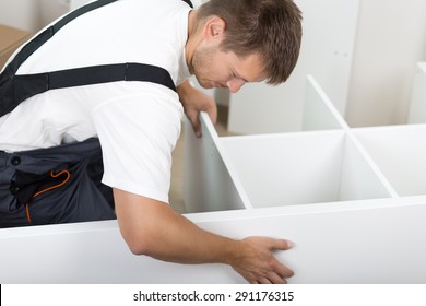 Man Dressed In Workers' Overall Assembling Furniture Sitting On The Floor In New Home. DIY, Home And Moving Concept