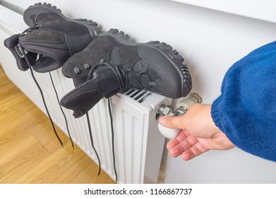 Man dries wet winter shoes on the heater at home. Part of body, selective focus.