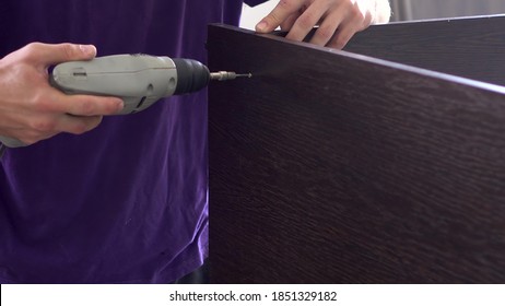 A Man Drills A Hole In Wooden Planks In A Furniture Manufacturing Facility.