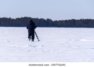 Man Drills Holes In The Ice For Ice Fishing With An Electric Auger. Selective Focus