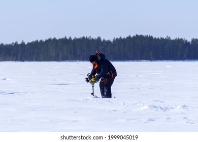 Man Drills Holes In The Ice For Ice Fishing With An Electric Auger. Selective Focus