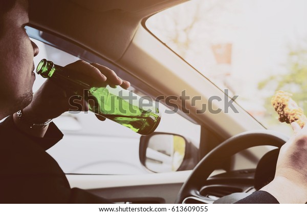 Man drinking beer and eating fried chicken while\
driving a car