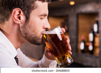 Man drinking beer. Side view of handsome young man drinking beer while sitting at the bar counter  - Powered by Shutterstock