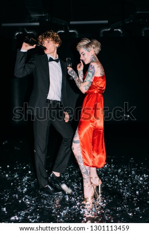 man drinking from bottle while standing near woman with glass of alcohol drink on party isolated on black
