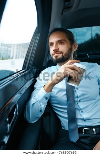 Man Drinking Coffee In Car. Portrait Of\
Successful Confident Smiling Businessman Drinking Hot Drink In Cup,\
Looking Through Window While Riding On Back Seat Of Car, Going To\
Work. High Resolution