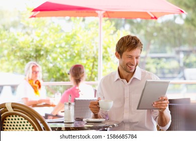 Man drinking coffee looking at digital tablet in outdoor caf_