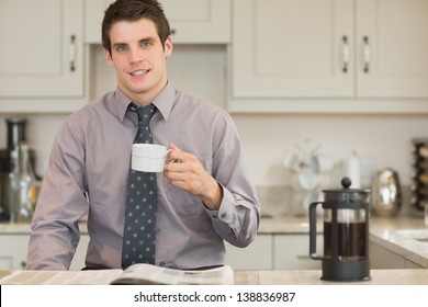 Man Drinking Coffee While Reading Newspaper In Kitchen