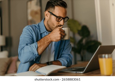 Man drinking coffee while working remotely on his laptop, enjoying a productive day in his home office