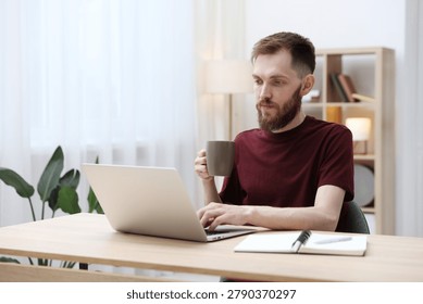 Man drinking coffee while working with laptop at wooden table indoors