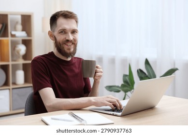Man drinking coffee while working with laptop at wooden table indoors