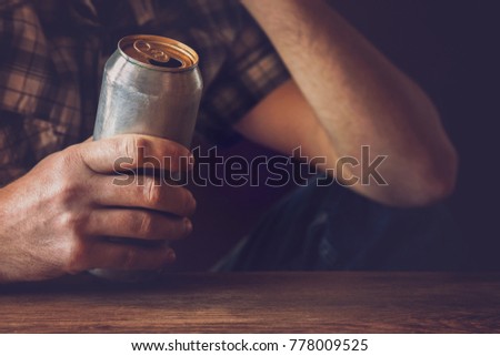 Man drinking a cold beer after work in the evening. Hand holding a aluminum can. Resting time in the bar or pub. Thoughtful atmosphere. Alcohol problem concept.