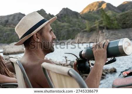 Man drinking mate by mountain lake with thermos and straw hat