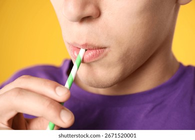 Man drinking refreshing drink through straw on orange background, closeup