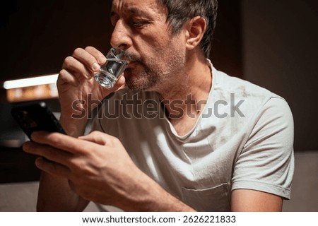 Man drinking vodka and using mobile phone, selective focus