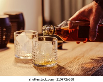 Man Drinking Whiskey At Home. Man Pouring Whiskey Over Ice Cubes At Wooden Counter Bar, Drinking At Home Night Time. Drink Together After Work At Home. 