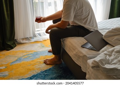 A Man Drinks Alcohol In A Hotel Room Or At Home. Tasting Of Spirits Such As Scotch, Brandy Or Whiskey. Young Businessman Under Stress In The Bedroom