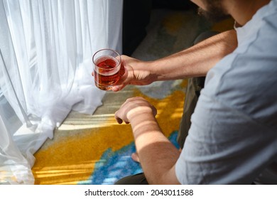 A Man Drinks Alcohol In A Hotel Room Or At Home. Tasting Of Spirits Such As Scotch, Brandy Or Whiskey. Young Businessman Under Stress In The Bedroom