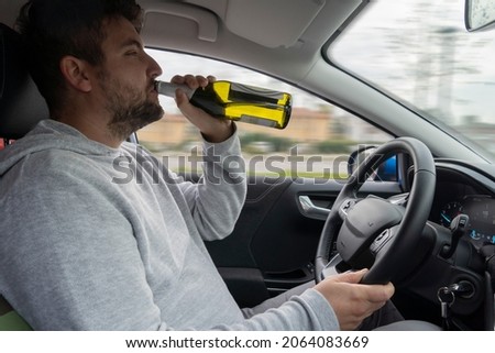 Man drinks alcohol while driving the car. Irresponsible behavior