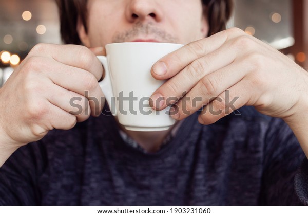 A man drinks coffee in a cafe, a restaurant. Brown\
interior, natural sunlight, blurred background, sideways. Snack,\
breakfast. Lunch break.