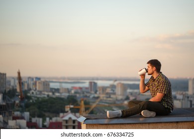 A man drinks coffee early in the morning on the roof. He looks away and thinks. In the background, the city landscape - Powered by Shutterstock