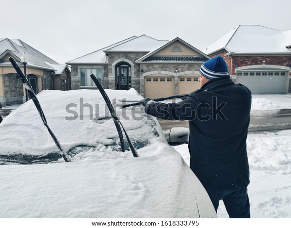 Man driver cleaning car front window from ice and snow\
with scraper.  Problems of bad winter north weather snowstorm cold\
climate. 